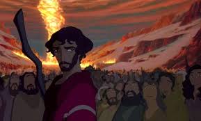 Un homme animé se tient devant une foule tandis qu’une immense colonne de feu s’élève dans un paysage montagneux dramatique.