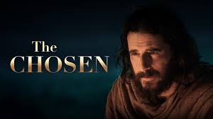 Un homme barbu vêtu simplement est éclairé dans l’obscurité, avec le titre « The Chosen » à côté de lui.